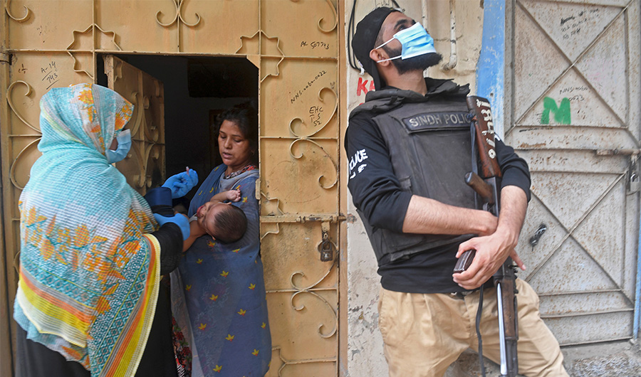 A policeman stands guard as a health worker (L) administers polio vaccine drops to a child during a polio vaccination door-to-door campaign in Pakistan's port city of Karachi on July 20, 2020. ( AFP Photo)
