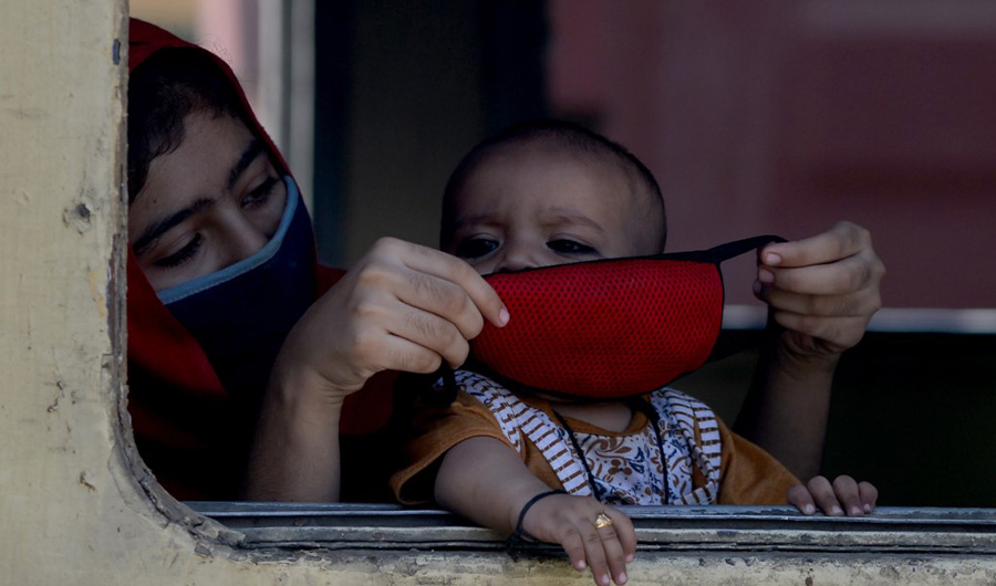 A passenger puts on a facemask on her child while waiting for their train to depart in Karachi on May 20, 2020. (AFP/File)