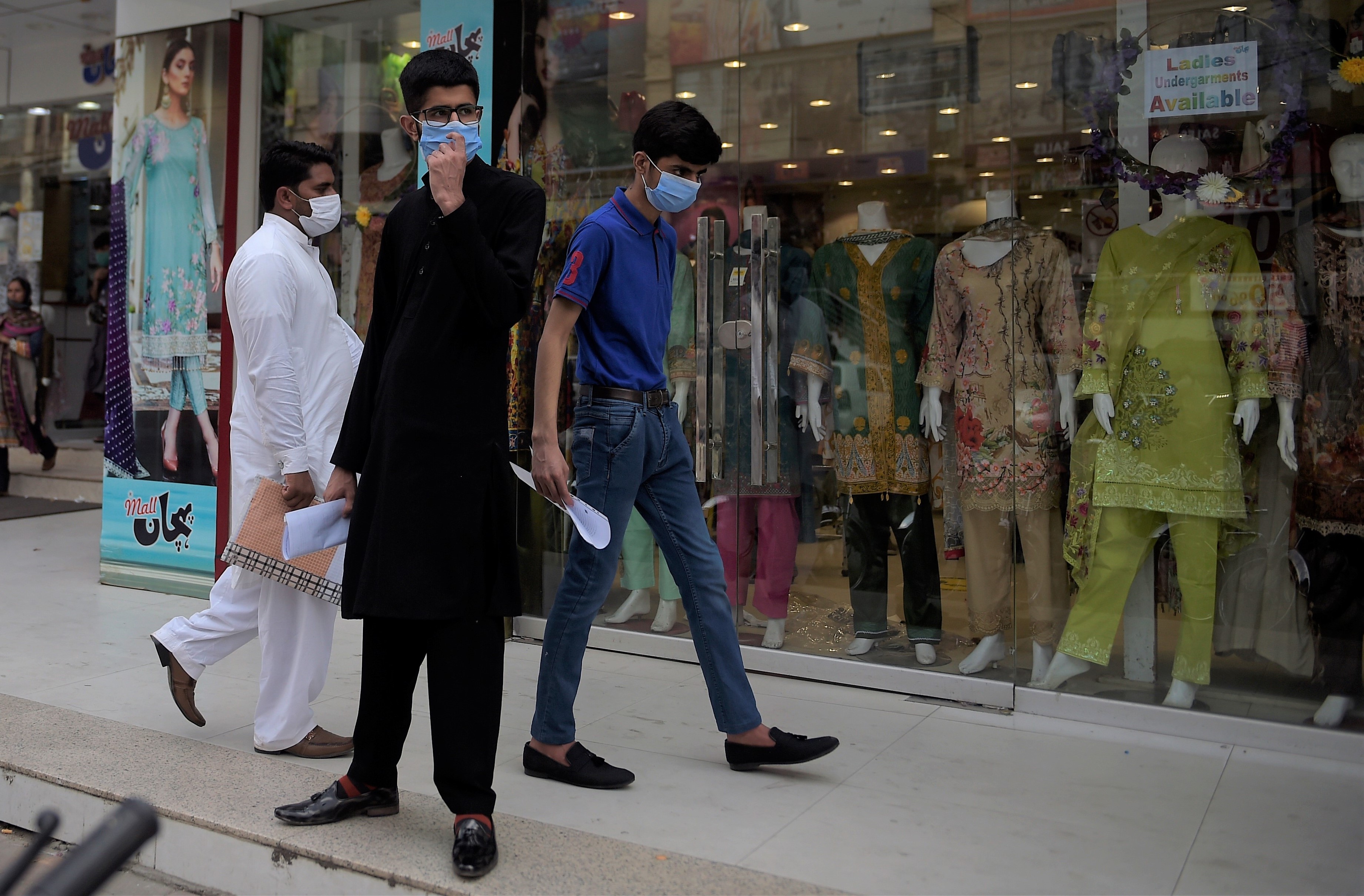 People wearing facemasks walk in front of a shopping mall in Rawalpindi on July 28, 2020, after Punjab province government announced to closed markets, shopping malls and plazas to contain the spread of Covid-19 corona virus on the occasion of the Muslim festival Eid al-Adha. (AFP)