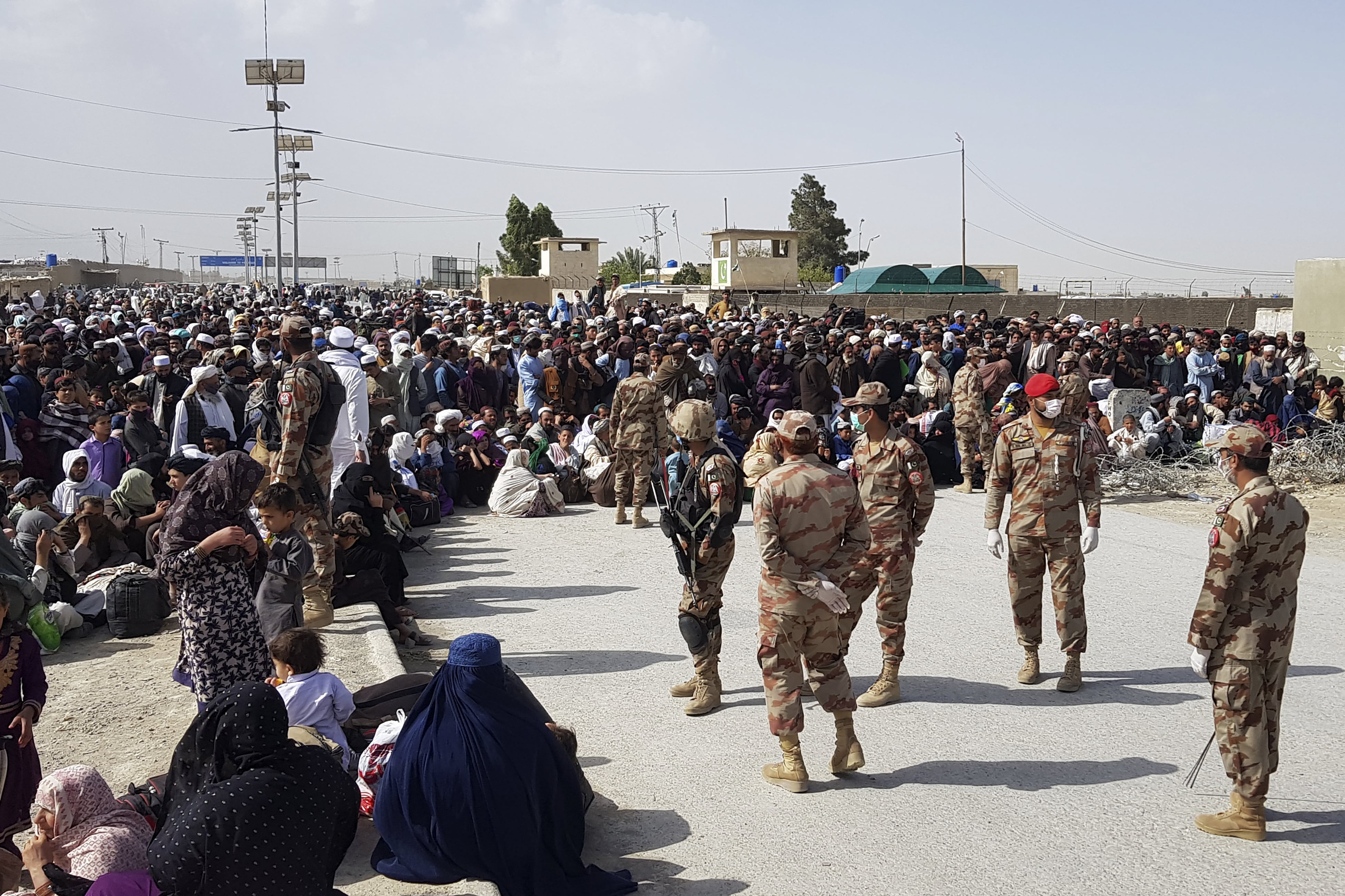 Afghan nationals wait to cross Pakistan and Afghanistan border as security personnel wearing facemasks stand beside them during a government-imposed nationwide lockdown as a preventive measure against the COVID-19 coronavirus, at the Pakistan's border town of Chaman on April 7, 2020. (AFP)