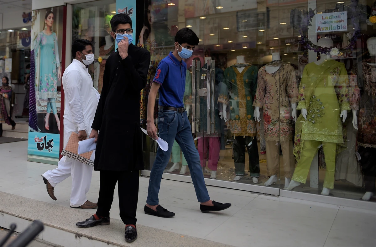 People wearing facemasks walk in front of a shopping mall in Rawalpindi on July 28, 2020, after Punjab province government announced to closed markets, shopping malls and plazas to contain the spread of Covid-19 corona virus on the occasion of the Muslim festival Eid al-Adha. (AFP)