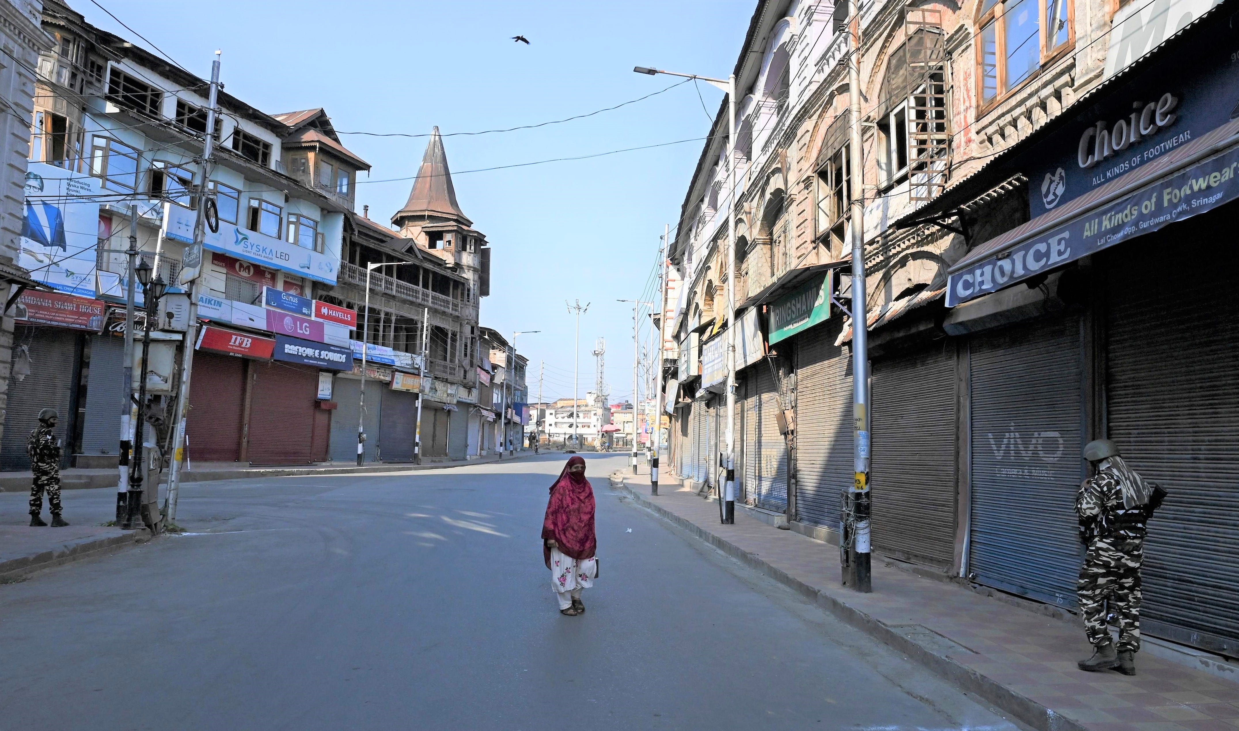 A woman walks along a street as security personnel stand guard during the one-year anniversary of the restive Kashmir region being stripped of its autonomy in Srinagar on August 5, 2020. (AFP)