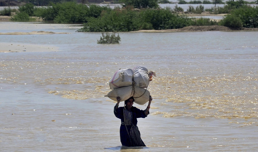 A woman carries sack of wheat and household goods while she wades through a flooded area of Dadu, a district in the Pakistan's southern Sindh province, Sunday, Aug. 9, 2020. (AP)