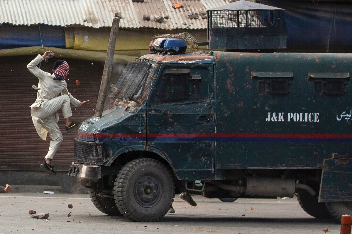 A masked Kashmiri protester jumps on an armored Indian police vehicle while throwing stones during a protest in Srinagar on May 31, 2019. (AP)
