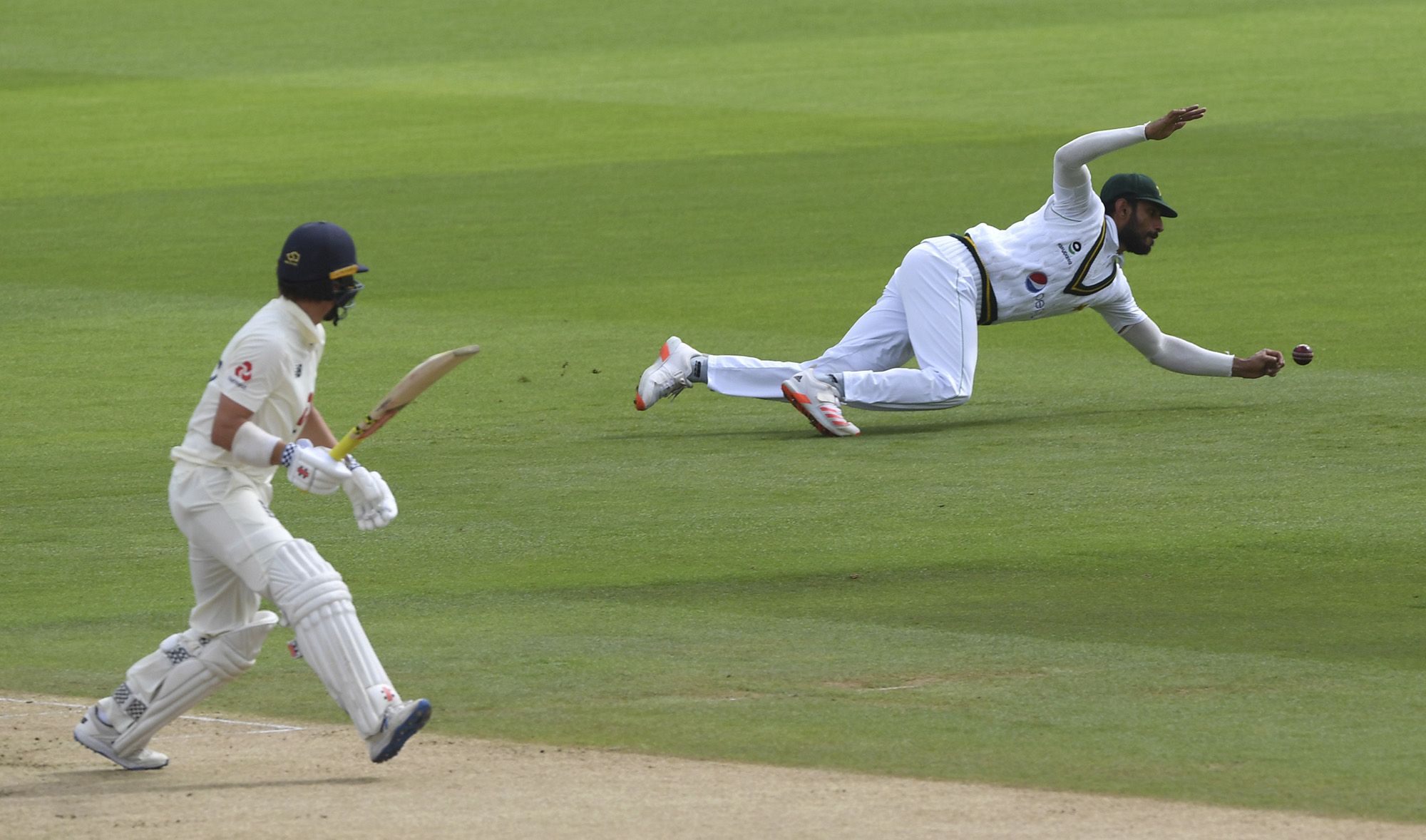 Pakistan's Shan Masood, right, dives to field the ball after a shot played by England's Rory Burns, left, during the first day of the third cricket Test match between England and Pakistan, at the Ageas Bowl in Southampton, England on Aug. 21, 2020. (Pool via AP)