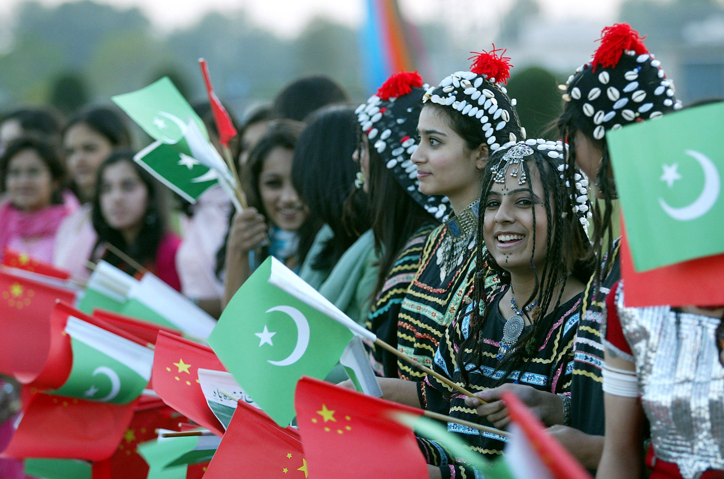 Pakistani girls wearing traditional costume wave Pakistani and Chinese flags as they line up in front of an aircraft of the Chinese president arriving for a state visit to Pakistan, at the Chaklala Airbase in Rawalpindi on Nov. 23, 2006. (AFP/File)