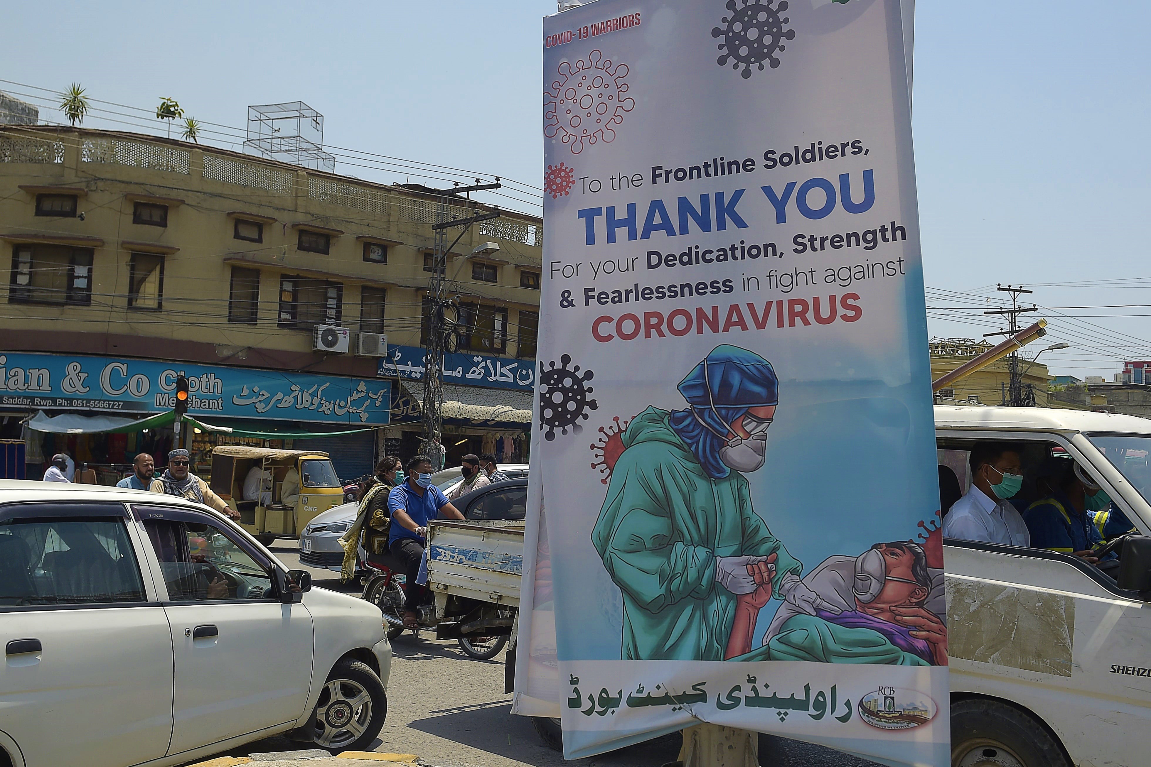 Commuters ride past a poster that shows gratitude to frontline workers fighting against the spread of the COVID-19 coronavirus, in Rawalpindi on June 30, 2020. (AFP)
