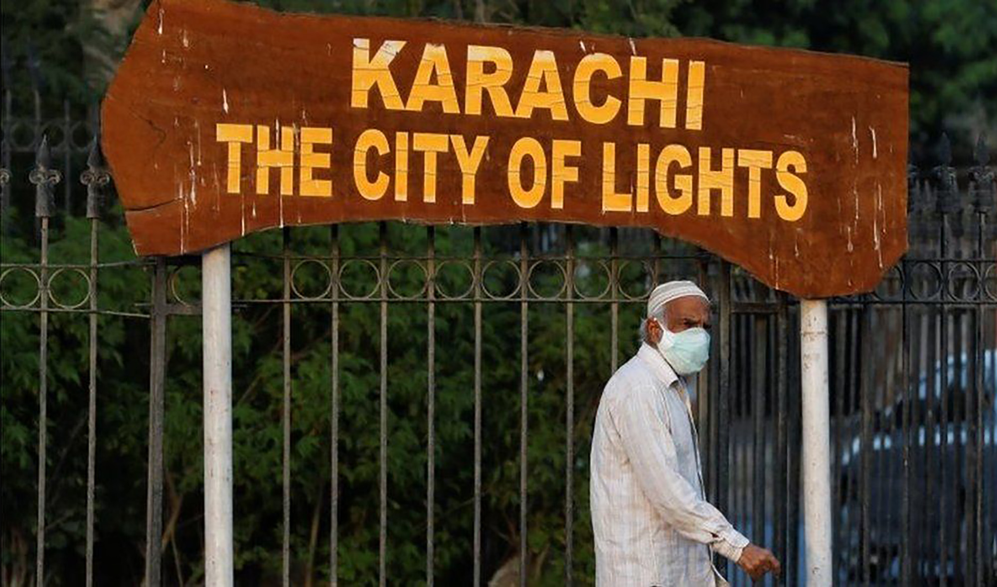 A man walks beside a sign along a road wearing a protective mask as a precaution against COVID-19 in Karachi on July 1, 2020. (REUTERS/File)