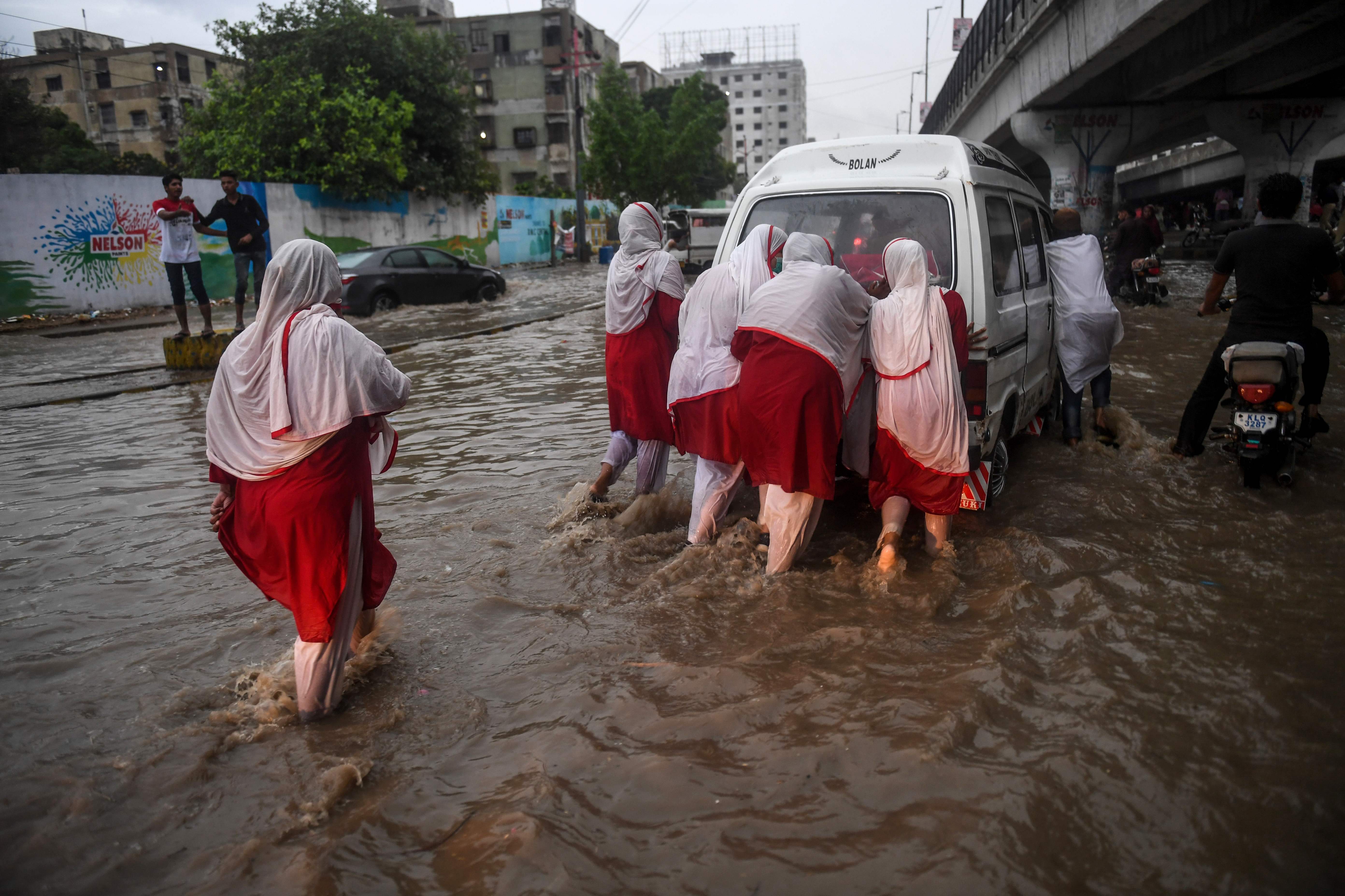 Pedestrians push a vehicle through a flooded street after heavy monsoon rains in Karachi on Aug. 21, 2020 (AFP)