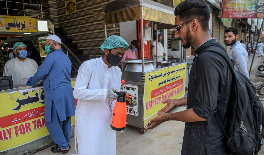 An employee (C) sanitizes the hands of a customer outside a restaurant open for takeaway and delivery services during a government-imposed nationwide lockdown as a preventive measure against the COVID-19 coronavirus, in Karachi on April 18, 2020. (AFP)