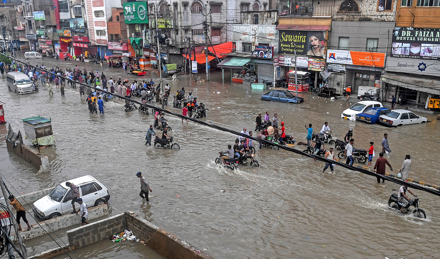 Motorists and pedestrians wade through a flooded street after heavy monsoon rains in Pakistan's port city of Karachi on Aug. 27, 2020. (AFP)