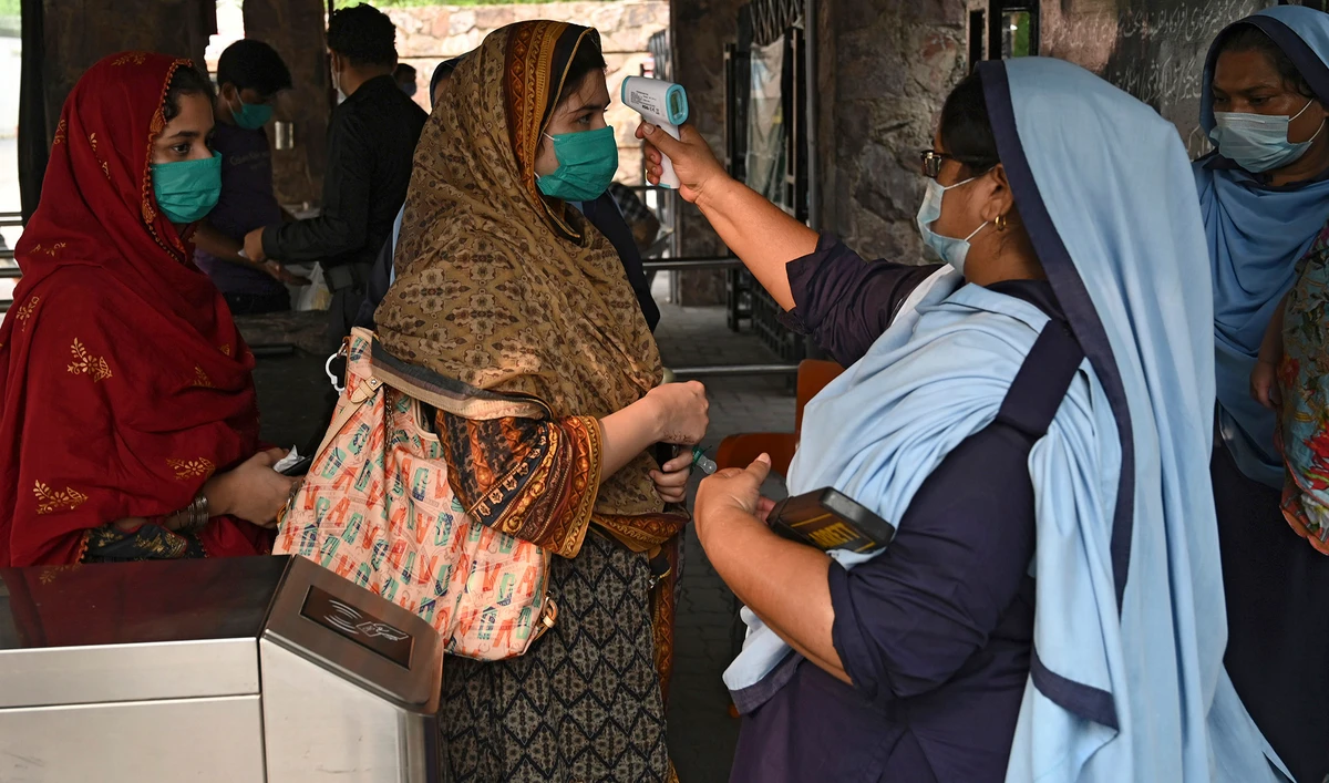 An official, right, checks the body temperature of a woman before entering at a Zoo in Lahore on Aug. 11, 2020. (AFP)