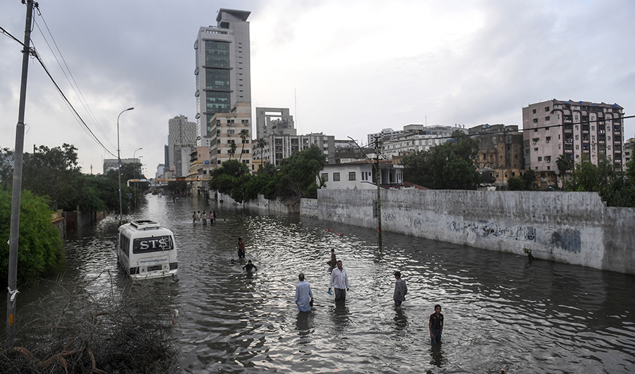 Pedestrians and motorists cross the main flooded I. I. Chundrigar Road is located in central business district of Karachi on August 28, 2020, after heavy monsoon rains triggered floods. (AFP)