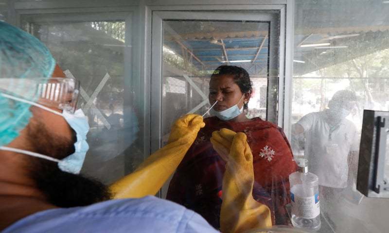 A paramedic wearing protective gear takes a nasal swab of a woman at a glass booth, to be tested for Covid-19 in Karachi, Pakistan on July 15, 2020. (Reuters)