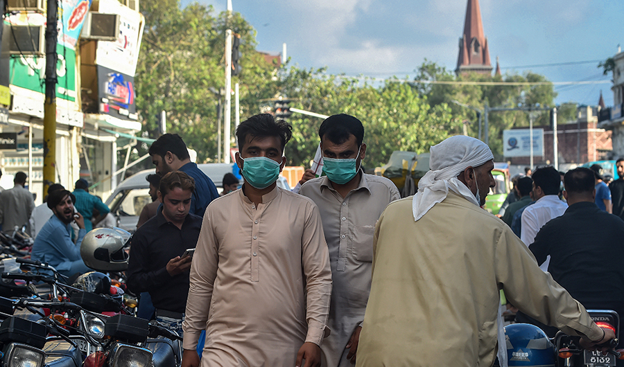 In this picture taken on August 31, 2020, men wearing facemasks as a preventive measure against the Covid-19 coronavirus walk through a market in Lahore. (AFP)