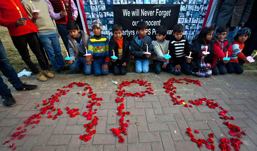 Pakistani youth hold candles next to a banner showing pictures of victims of an attack on a Peshawar school in 2014 during a demonstration in connection with the first anniversary of the attack on Dec. 15, 2015. (AP/File)