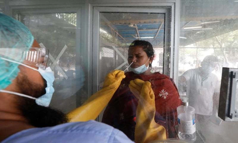 A paramedic wearing protective gear takes a nasal swab of a woman at a glass booth, to be tested for Covid-19 in Karachi, Pakistan on July 15, 2020. (Reuters)
