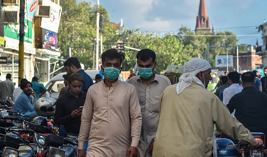 In this picture taken on August 31, 2020, men wearing facemasks as a preventive measure against the Covid-19 coronavirus walk through a market in Lahore. (AFP)
