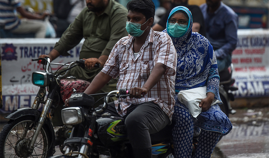 A couple wearing facemasks as a preventive measure against the COVID-19 coronavirus ride a bike on a street in the Pakistan's port city of Karachi on August 6, 2020. (AFP)