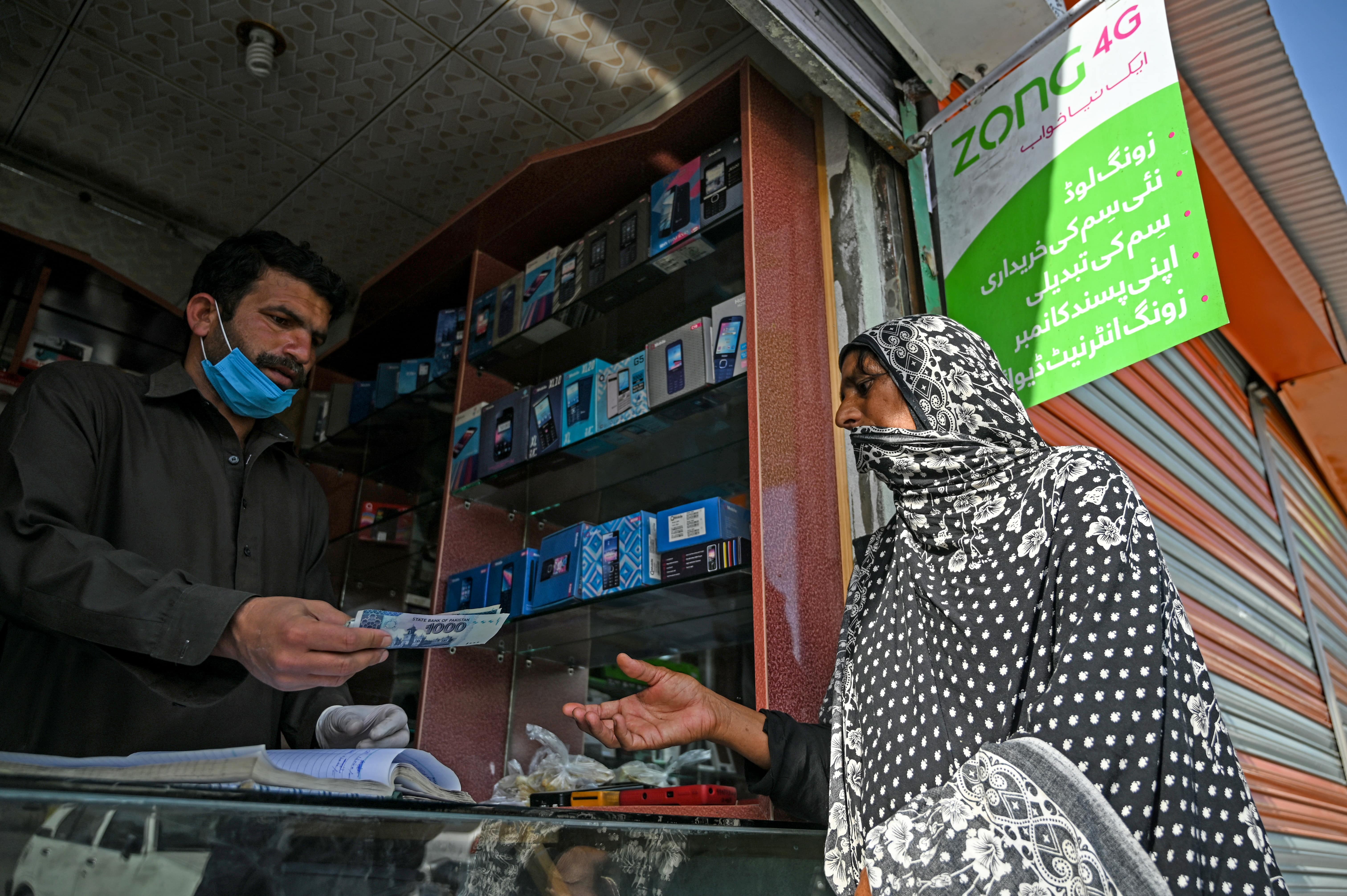 A woman (R) gets rupee notes as she collects cash of financial assistance through a mobile wallet under the governmental Ehsaas Emergency Cash Programme for families in need during a government-imposed nationwide lockdown as a preventive measure against the COVID-19 coronavirus, in Islamabad on April 9, 2020. (AFP)