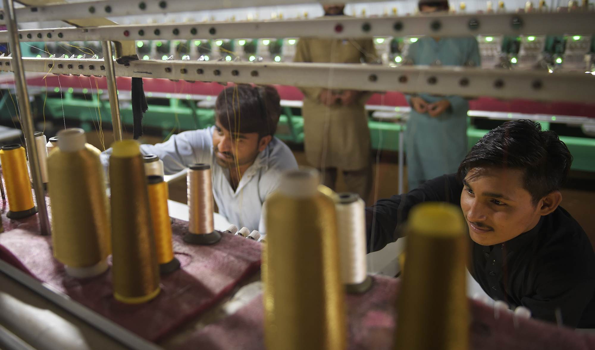 Workers supervise embroidery machines working on fabrics for wedding dresses at a small factory on the outskirts of Islamabad on Sept. 2, 2020. (AFP)