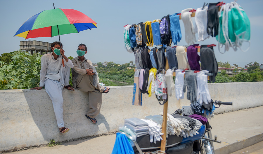 Street vendors selling facemasks sit under an umbrella as they wait for customers on a roadside after the government eased the lockdown imposed as a preventive measure against the COVID-19 coronavirus, in Rawalpindi on May 9, 2020 (AFP)