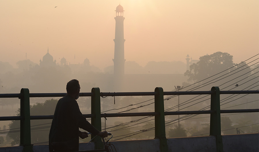 In this picture taken on December 6, 2019, a man walks with a bicycle along a bridge amid heavy smog conditions near Badshahi Mosque in Lahore. (AFP)