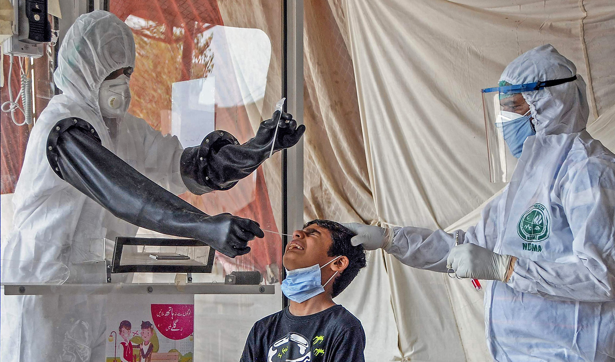 Health officials wearing protective gear take a nasal swab sample from a young boy, center, at a screening and testing facility for the COVID-19 coronavirus, in Hyderabad on June 26, 2020, some 160 kms east of the southern port city of Karachi. (AFP/File)