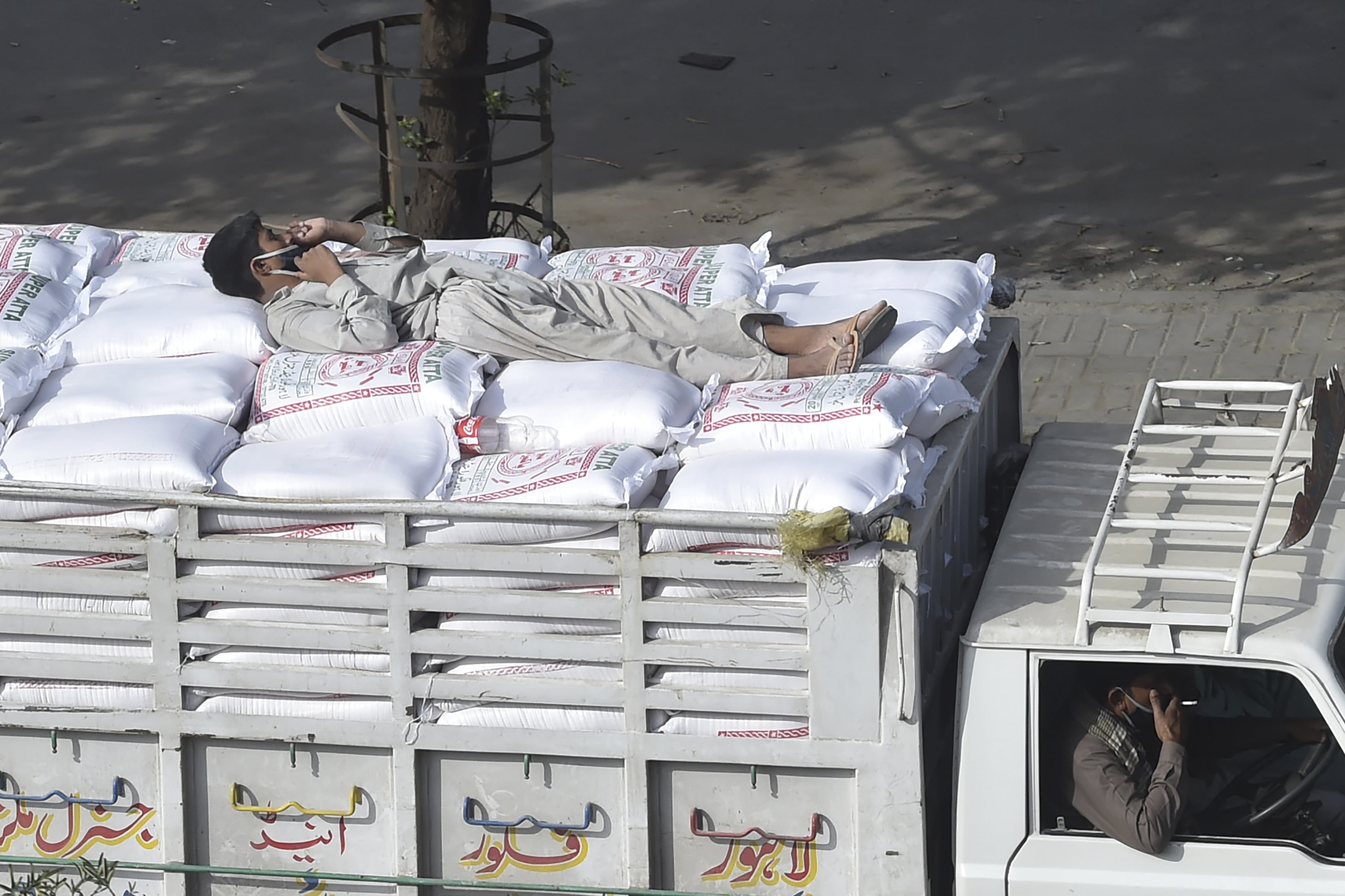 A worker wearing a facemask lies on wheat bags on top of a loaded mini truck on a street during a government-imposed nationwide lockdown as a preventive measure against the COVID-19 coronavirus, in Lahore on April 6, 2020. (AFP)