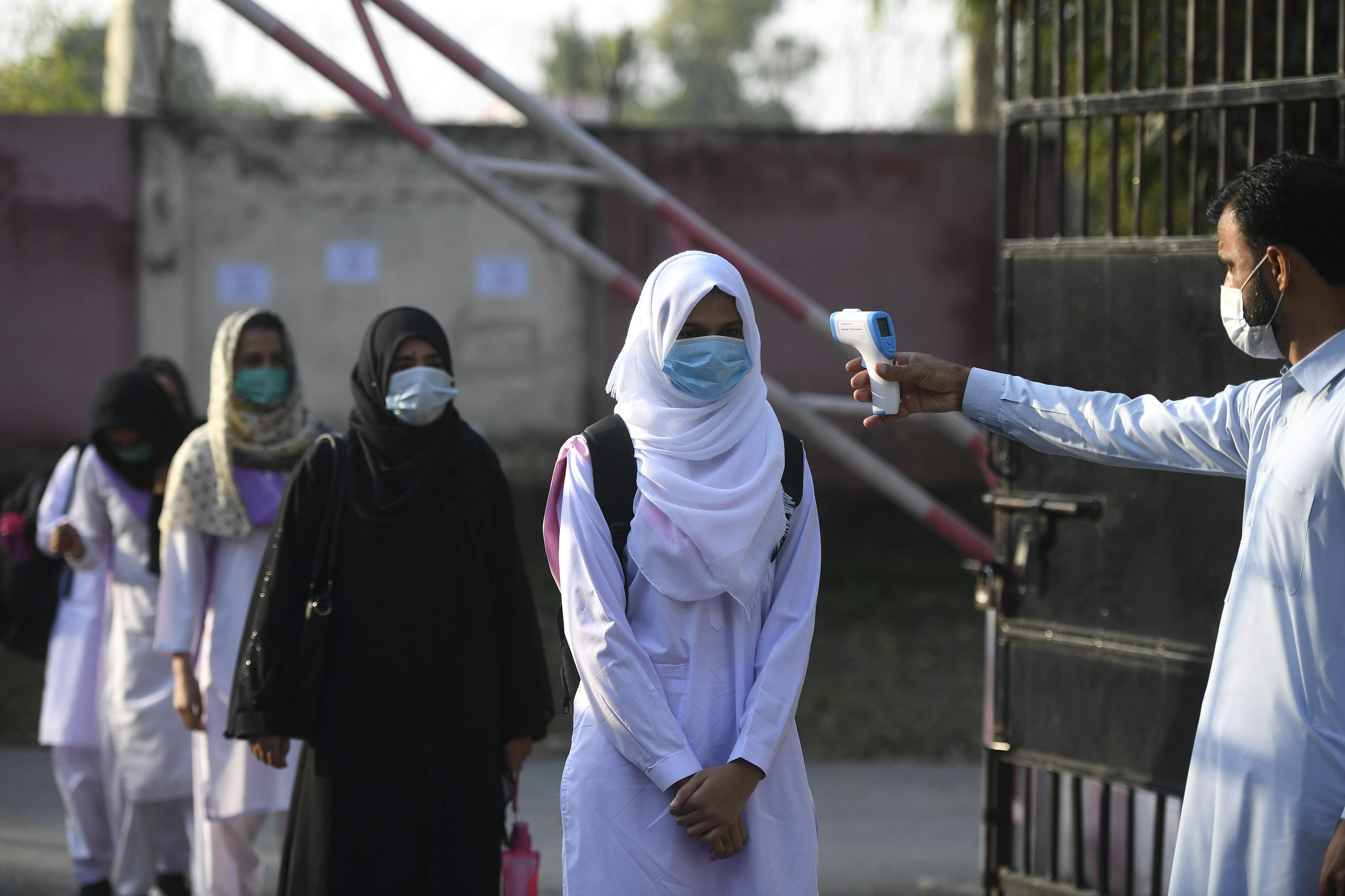 A staff member checks the body temperature of students at the entrance of the Islamabad Model College of Commerce for Girls in Islamabad on September 15, 2020 after the educational institutes were reopened nearly six months after the spread of the Covid-19 coronavirus. (AFP)
