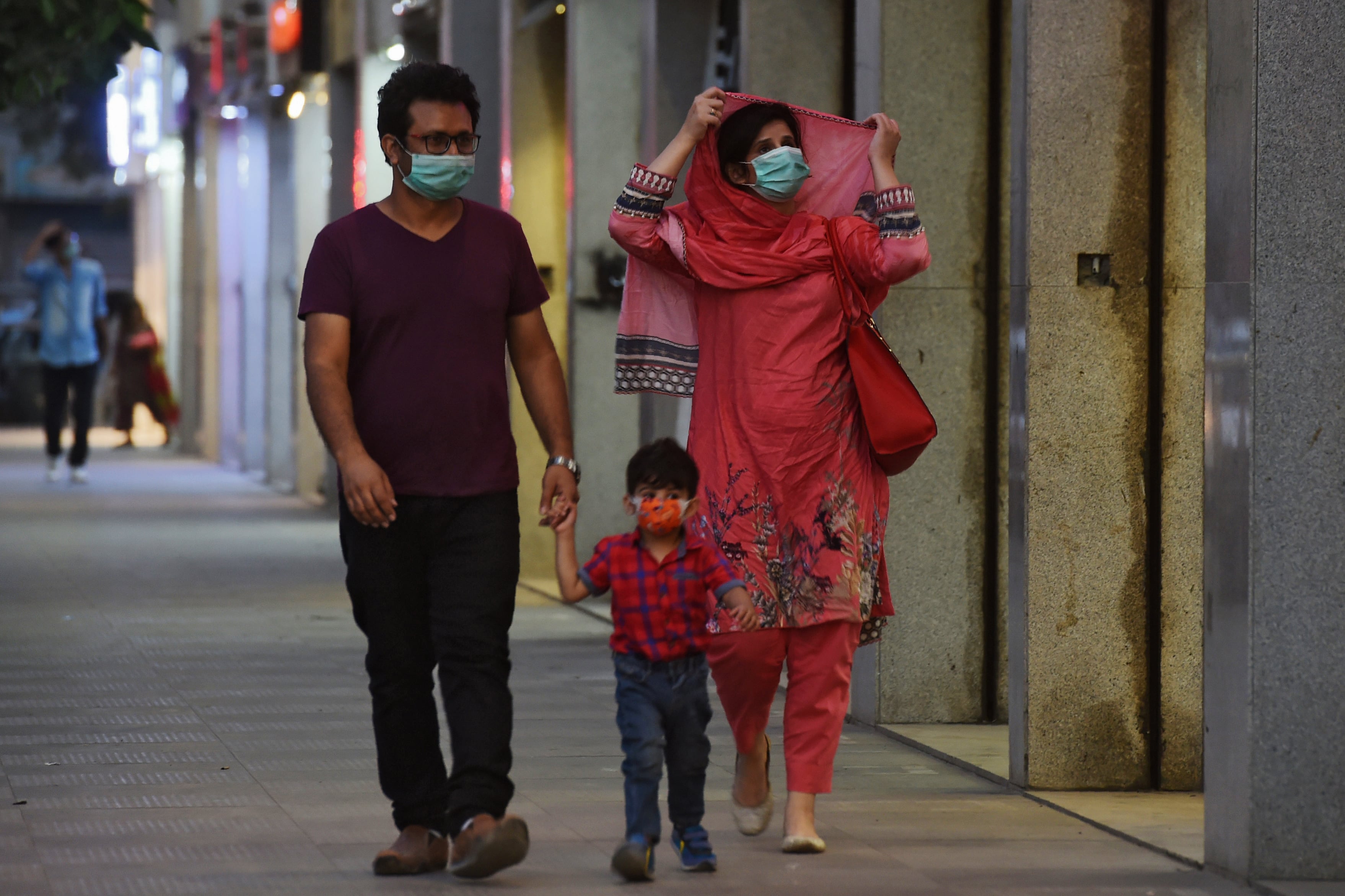 A family wearing facemasks as a preventive measure against the Covid-19 coronavirus walk along side a street, in Karachi on October 29, 2020. (AFP)