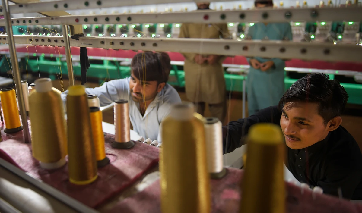 Workers supervise embroidery machines working on fabrics for wedding dresses at a small factory on the outskirts of Islamabad on Sept. 2, 2020. (AFP)