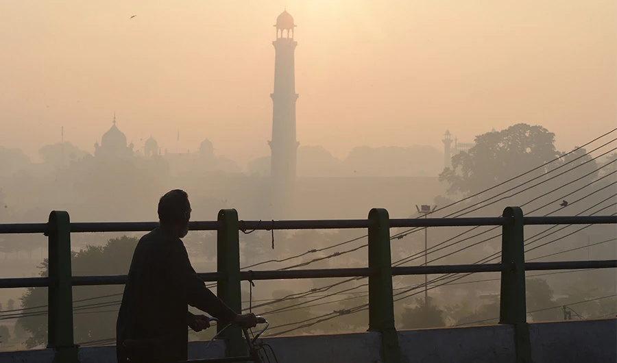 In this picture taken on December 6, 2019, a man walks with a bicycle along a bridge amid heavy smog conditions near Badshahi Mosque in Lahore. (AFP)