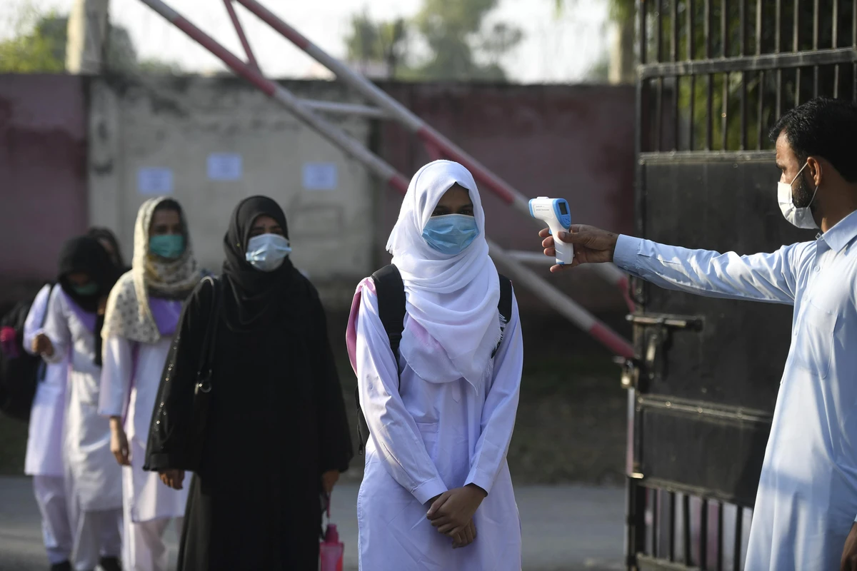 A staff member checks the body temperature of students at the entrance of the Islamabad Model College of Commerce for Girls in Islamabad on September 15, 2020 after the educational institutes were reopened nearly six months after the spread of the Covid-19 coronavirus. (AFP)