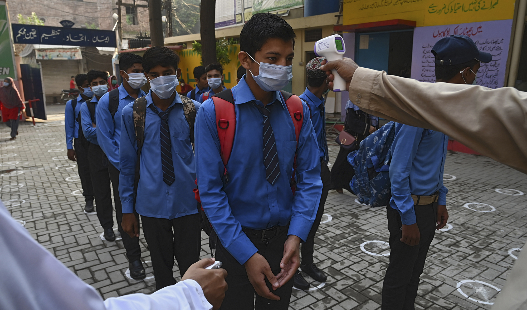 A teacher checks the body temperature of students at a government school in Lahore on Sept. 15, 2020 after the educational institutes were reopened nearly six months after the spread of the Covid-19 coronavirus. (AFP/File)