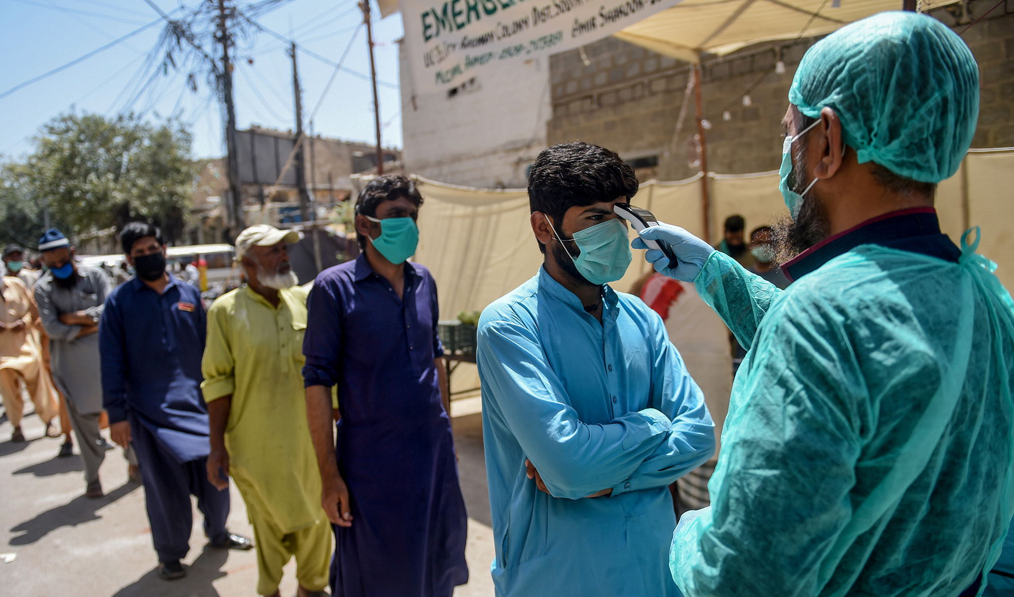 A municipal worker, right, checks the body temperature of a man queuing along with other people at a low-rate food distribution point during a government-imposed nationwide lockdown as a preventive measure against the COVID-19 coronavirus, in Karachi on April 4, 2020. (AFP/File)