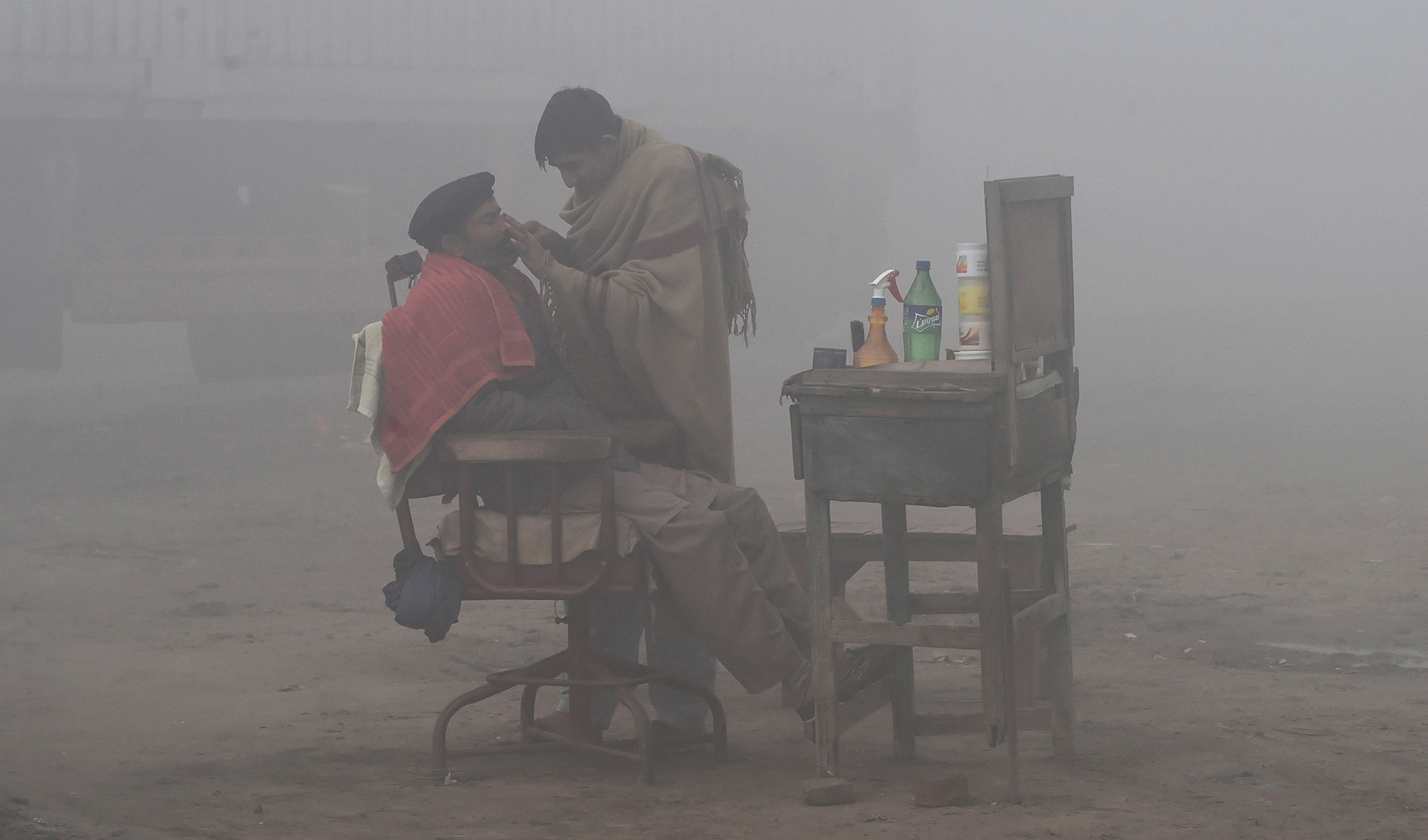 A Pakistani barber shaves a customer alongside a road amid heavy fog and smog conditions in Lahore on Jan. 24, 2019. (AFP/File)