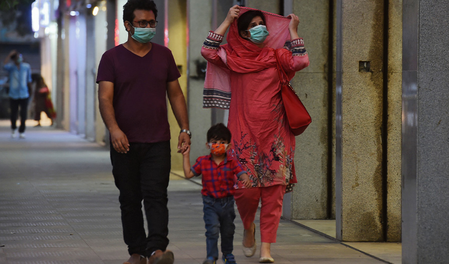 A family wearing facemasks as a preventive measure against the Covid-19 coronavirus walk along side a street, in Karachi on October 29, 2020. (AFP)