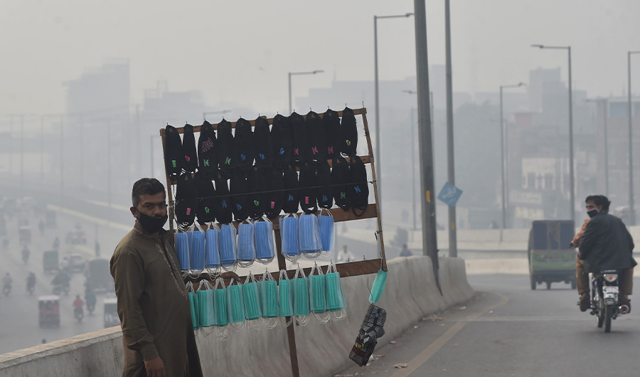A vendor selling facemasks waits for customers on a bridge amid heavy smoggy conditions in Lahore on November 10, 2020. (AFP)