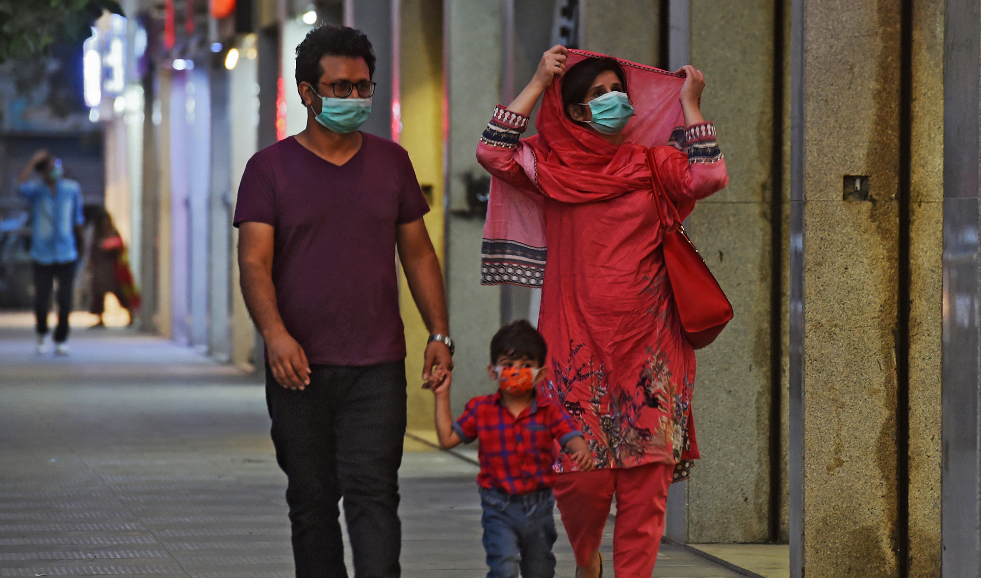 A family wearing facemasks as a preventive measure against the Covid-19 coronavirus walk along side a street, in Karachi on Oct. 29, 2020. (AFP/File)