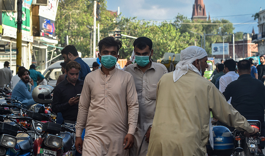 In this picture taken on August 31, 2020, men wearing facemasks as a preventive measure against the Covid-19 coronavirus walk through a market in Lahore. (AFP)