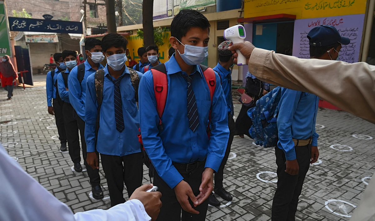A teacher checks the body temperature of students at a government school in Lahore on Sept. 15, 2020 after the educational institutes were reopened nearly six months after the spread of the Covid-19 coronavirus. (AFP/File)