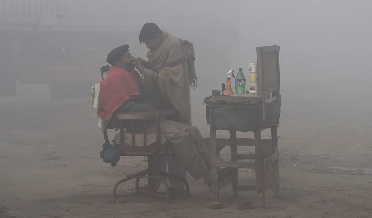 A Pakistani barber shaves a customer alongside a road amid heavy fog and smog conditions in Lahore on Jan. 24, 2019. (AFP/File)