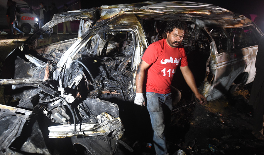 FILE - A volunteer walks past a burnt passenger van following an overnight accident in the Nooriabad area on a highway some 50 kilometers from Pakistan's port city of Karachi late on September 26, 2020. (AFP)