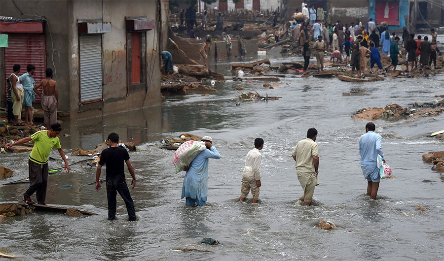 People wade through a flooded residential area after heavy monsoon rains in Pakistan's port city of Karachi on August 27, 2020 (AFP)
