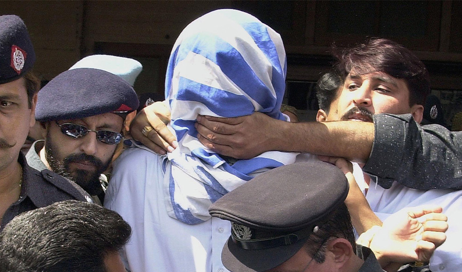 A Pakistani policeman (R) tries to cover the mouth of British-born Pakistani militant Sheikh Omar (C) as he tries to shout a message to the press outside a Pakistani court in Karachi, 12 March 2002.(AFP/ File photo)