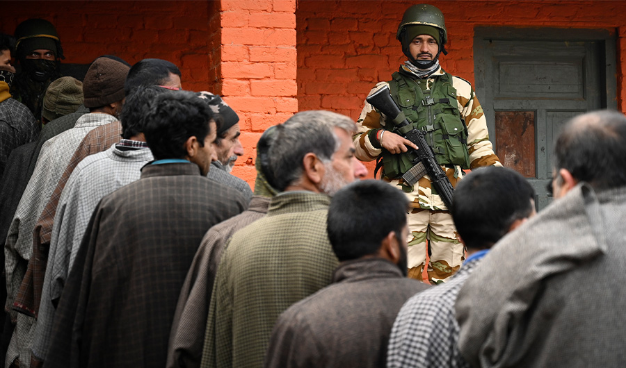 An Indian paramilitary soldier stands guard as voters stand in a queue to cast their ballots during the second phase of the District Development Council (DDC) and Panchayat by-elections at a polling station in Najan Sumbal area of Bandipora district on December 1, 2020. (AFP)