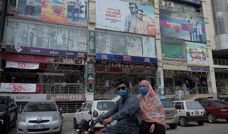 A family rides past a shoppig mall in Rawalpindi on July 28, 2020, after Punjab province government announced to closed markets, shopping malls and plazas to contain the spread of Covid-19 coronavirus on the occasion of the Muslim festival Eid al-Adha. (AFP)