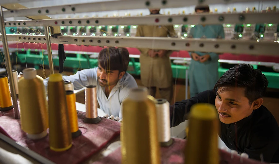 Workers supervise embroidery machines working on fabrics for wedding dresses at a small factory on the outskirts of Islamabad on September 2, 2020. (AFP)