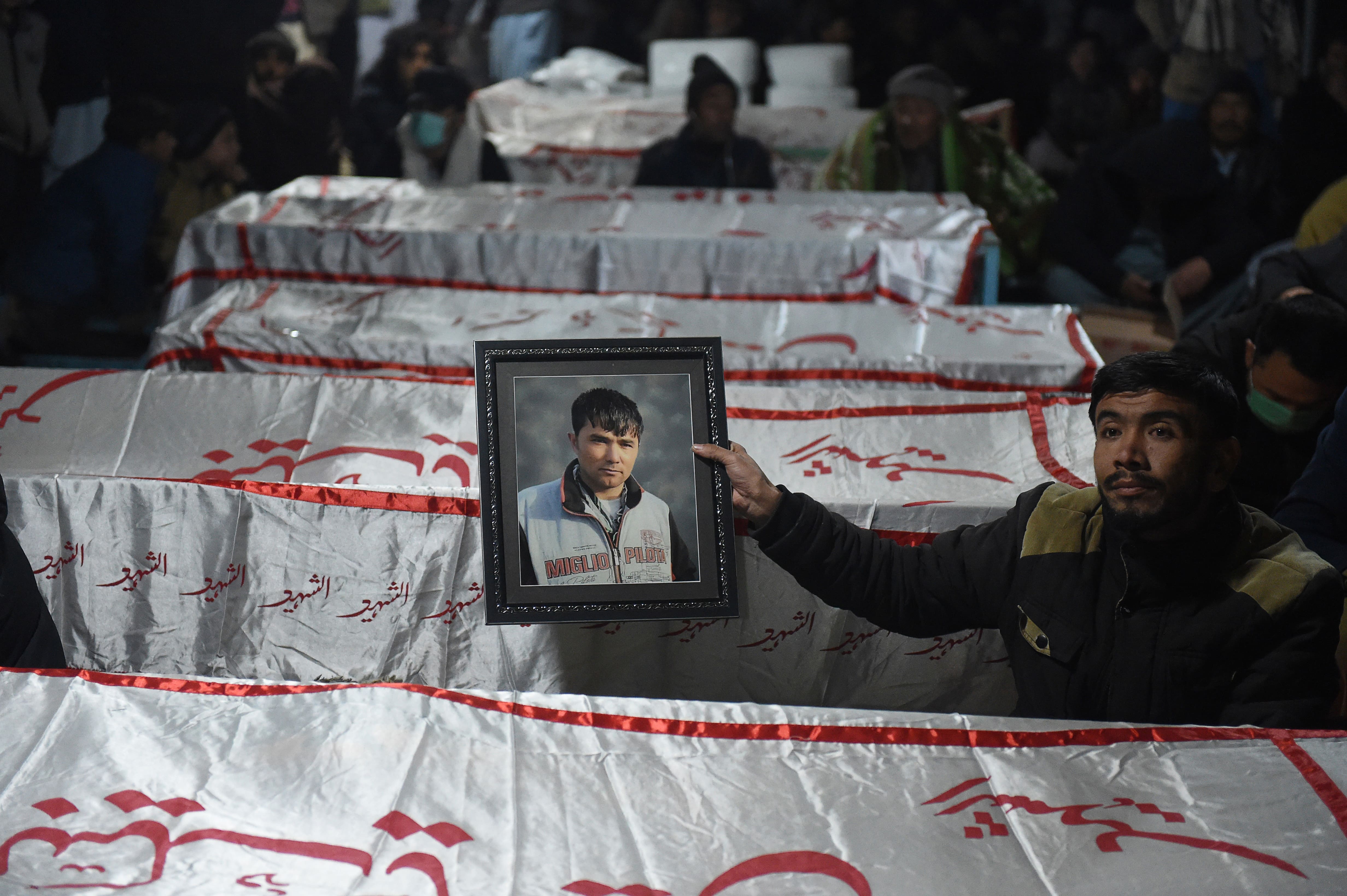 A mourner from a Shiite Hazara community holds a photograph of a victim near the coffins of other miners who were killed in an attack by gunmen in the mountainous Machh area, on the outskirts of Quetta on January 4, 2021. (AFP)